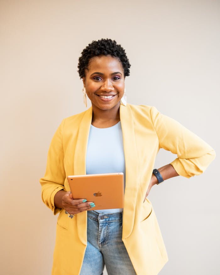Professional African American woman smiling and holding a tablet indoors, exemplifying modern business attire.